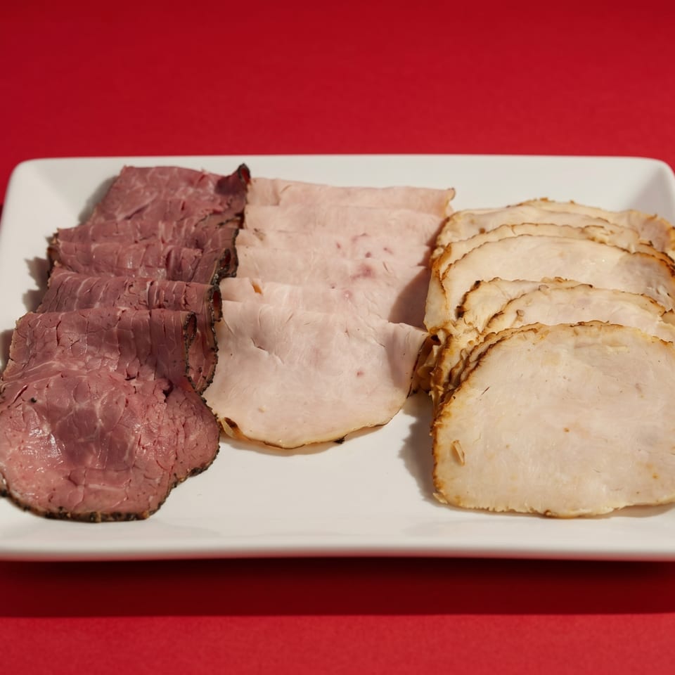 A white rectangular platter holds three rows of sliced deli meats: roast beef, ham, and turkey.