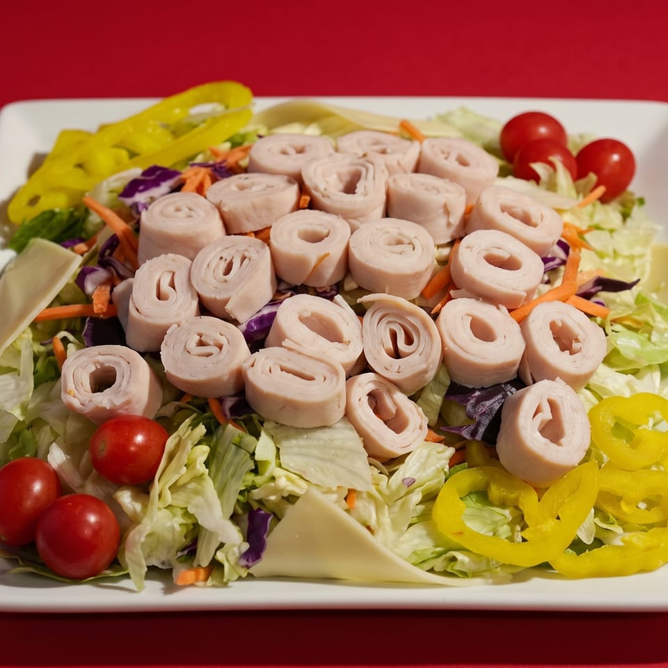 A chef salad with rolled turkey, cherry tomatoes, yellow peppers, and cheese on a white plate.